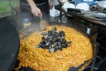 D'en haut des gars des cultures en tenue décontractée cuisson rue paella avec des moules dans la stalle du marché — Photo de stock