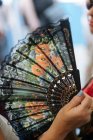 Crop lady with colourful fan with flowers in hand in market stall — Stock Photo