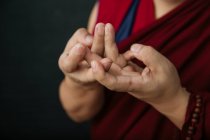 Primo piano delle mani del raccolto pregando monaco tibetano in tradizionale veste rossa con mudra gesto simbolico mani — Foto stock