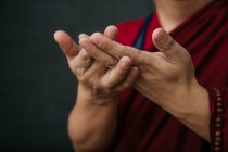 Закрытие рук урожая молящегося тибетского монаха в традиционном красном халате с мудрой символической рукой жестом — стоковое фото