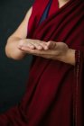 Primer plano de las manos de la cosecha rezando monje tibetano en túnica roja tradicional con gesto de manos simbólicas mudra - foto de stock
