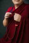 Vue latérale du moine bouddhiste en vêtements rouges traditionnels tenant des perles de prière à la main — Photo de stock