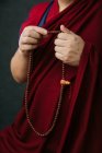 Вид сбоку на урожай буддийский монах в традиционной красной одежде с молитвенными бусами в руке — стоковое фото