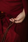 Vista lateral da colheita monge budista em roupas vermelhas tradicionais segurando contas de oração na mão — Fotografia de Stock