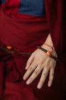 Vue latérale du moine bouddhiste en vêtements rouges traditionnels tenant des perles de prière à la main — Photo de stock