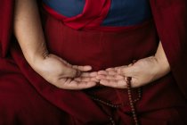 Vista lateral de la cosecha monje budista en ropa roja tradicional sosteniendo cuentas de oración en la mano - foto de stock