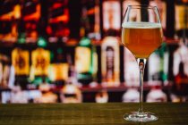 Пиво в бокале с пеной в стекле на деревянном прилавке в баре на фоне размытости — стоковое фото