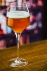 Birra in bicchiere da vino con schiuma in vetro su bancone in legno su sfondo sfocato — Foto stock