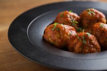 De cima saborosas almôndegas cozidas com molho de tomate servindo com pão em prato preto com talheres e bebidas na mesa — Fotografia de Stock
