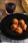De cima saborosas almôndegas cozidas com molho de tomate servindo com pão em prato preto com talheres e bebidas na mesa — Fotografia de Stock