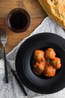 Von oben leckere gekochte Fleischbällchen mit Tomatensauce, dazu Brot auf schwarzem Teller mit Besteck und Getränken auf dem Tisch — Stockfoto