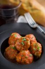 Von oben leckere gekochte Fleischbällchen mit Tomatensauce, dazu Brot auf schwarzem Teller mit Besteck und Getränken auf dem Tisch — Stockfoto