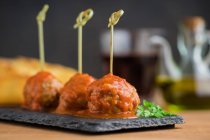 Boulettes de viande savoureuses avec sauce tomate collées avec des bâtons de bambou sur un plateau plat sur la table — Photo de stock