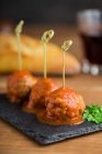 Tasty meat balls with tomato sauce bonded with bamboo sticks on flat board on table — Stock Photo
