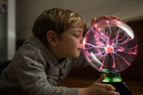 Мальчик смотрит на таинственную стеклянную лампу молнии на столе — стоковое фото