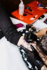 De cima cortado homem irreconhecível com o uso de máquina de tatuagem para fazer tatuagem na perna do cliente da colheita durante o trabalho no salão — Fotografia de Stock