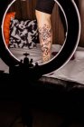 Crop unkenntlich Person Bein mit frischem Tätowieren in Runde glühende Lampe während Foto-Session im Tätowiersalon — Stockfoto