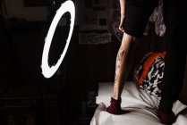 Обрізати невпізнавану ногу людини зі свіжим татуюванням в круглій світиться лампі під час фотосесії в татуювальному салоні — стокове фото