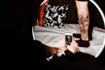 Tatuagem de homem irreconhecível usando smartphone para tirar foto de tatuagem na perna do cliente de colheita para portfólio no estúdio contemporâneo — Fotografia de Stock