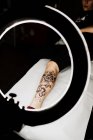 Cortar perna de mulher irreconhecível com tatuagem fresca em lâmpada brilhante redonda durante sessão de fotos no salão de tatuagem — Fotografia de Stock