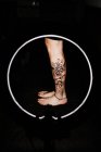 Cultiver jambe femme méconnaissable avec tatouage frais dans une lampe à incandescence ronde pendant la séance photo dans le salon de tatouage — Photo de stock
