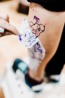 From above faceless tattoo artist removing transfer paper with tattoo from leg of client — Stock Photo