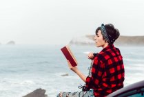 Femme décontractée réfléchie avec livre au bord de la mer — Photo de stock