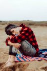 Femme hipster réfléchie assise sur une plage de sable — Photo de stock
