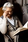 Elderly woman reading by window with enthusiasm — Stock Photo
