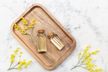 Dall'alto vista del fiore mimosa e il suo olio essenziale su vassoio di legno su tavolo di sfondo in marmo — Foto stock