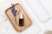 Top view lavender flower and its essential oil on a bottle drop at a marble table on wooden tray — Stock Photo
