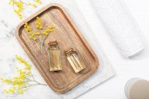 From above top view of mimosa flower and its essential oil on wooden tray on marble background table — Stock Photo