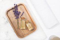 Lavendelblüte und ihr ätherisches Öl auf einer Flasche an einem Marmortisch auf einem Holztablett — Stockfoto