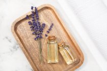 Top view fiore di lavanda e il suo olio essenziale su una bottiglia su un tavolo di marmo su un vassoio di legno — Foto stock