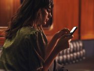Вид сбоку на стильную женщину с мобильным телефоном, удобно сидящую на черном кожаном диване в кафе — стоковое фото