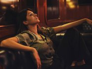 Вид сбоку усталой расслабленной женщины, опирающейся на спинку кожаного черного дивана и отводящей взгляд в кафе — стоковое фото