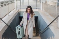 Сверху элегантная стильная молодая женщина-путешественница с чемоданом поднимается по лестнице на вокзале — стоковое фото