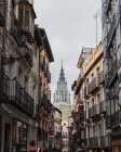 Знизу вузькою вулицею міста Толедо (Іспанія) зі старими житловими будинками та кафедральним собором на тлі сірого хмарного неба. — стокове фото
