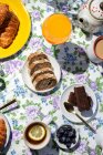 From above top view of homemade full brunch breakfast in sunlight with cooked eggs, blueberries, sponge cake, croissants, toast, tea, coffee and orange juice — Stock Photo