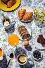 Сверху вид домашнего завтрака на солнце с приготовленными яйцами, черникой, бисквитом, круассанами, тостами, чаем, кофе и апельсиновым соком — стоковое фото
