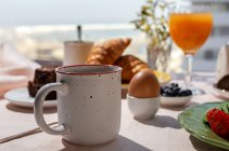 Homemade full brunch breakfast in sunlight with cooked eggs, blueberries, sponge cake, croissants, toast, tea, coffee and orange juice — Stock Photo