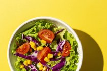 Свежий салат из салата с помидорами черри, красный лук и кукуруза, солнечный свет на розовом фоне сверху. Здоровое питание. Веганская еда . — стоковое фото