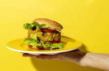 Ausgeschnittene unkenntliche Person hält einen hausgemachten veganen grünen Linsenburger mit Tomaten, Salat und Pommes auf gelbem Hintergrund — Stockfoto