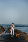 Femmina in abiti casual e grande marrone Mastiff cane guardando l'un l'altro mentre si cammina lungo il molo di legno bagnato contro l'acqua calma baia sotto il cielo blu in Spagna — Foto stock
