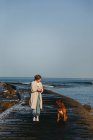 Feminino em roupas casuais e grande mastim marrom cão olhando um para o outro enquanto caminhava ao longo molhado cais de madeira contra a água calma baía sob céu azul na Espanha — Fotografia de Stock