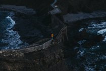 Сверху сзади вид человека с вытянутыми руками, наслаждающегося свободой, стоящего на старом каменном мосту против беспокойной воды с пеной, омывающей скалистые берега Испании — стоковое фото