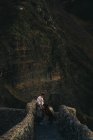 Vue latérale à angle élevé de la femelle en vêtements décontractés avec un grand chien brun debout sur un vieux pont en pierre et se regardant contre une pente rocheuse de montagne en Espagne — Photo de stock