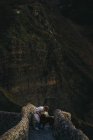 Vista laterale ad alto angolo di femmina in abiti casual con grande cane marrone in piedi sul vecchio ponte di pietra e guardando l'un l'altro contro pendio roccioso di montagna in Spagna — Foto stock