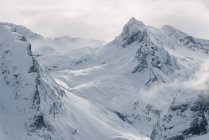 Суровый холодный зимний пейзаж со снежными скалистыми горными вершинами и солнечным светом, прорывающимся сквозь туман и снежную бурю — стоковое фото