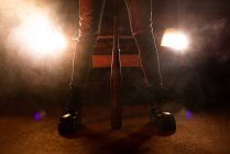 Crop Beine der gesichtslosen Frau in Jeans und schwarzen Stiefeln mit massiver Sohle hält Fledermaus mit Autoscheinwerfern auf dem Hintergrund — Stockfoto